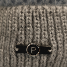 Load image into Gallery viewer, Close-up of a gray ribbed knit hat with a black bar and circular silver-tone metal charm featuring a white letter P.

