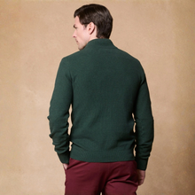 Load image into Gallery viewer, A man shown from the back wearing a dark forest green mock-neck knit sweater and burgundy trousers, standing against a textured tan studio backdrop.
