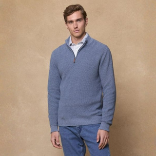 Man wearing a blue sweater and jeans against a beige background