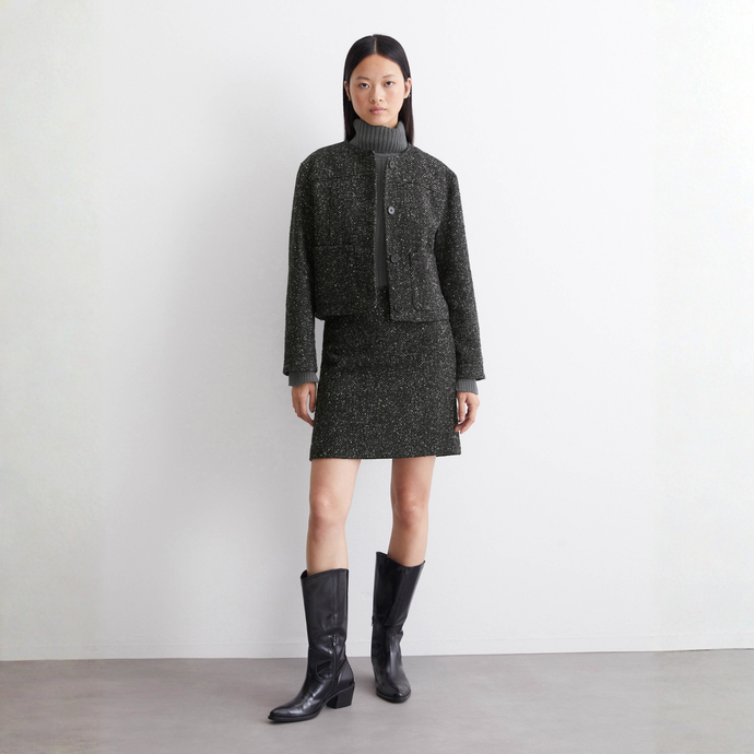 Woman wearing a dark gray outfit with a jacket and skirt, standing against a plain background.