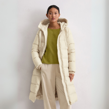 Load image into Gallery viewer, Person wearing a long beige puffer coat over a green sweater and beige pants on a light gray background
