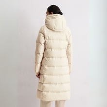 Load image into Gallery viewer, Person wearing a long beige puffer coat on a light gray background
