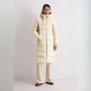 Person wearing a long beige puffer coat on a plain background