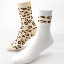 Load image into Gallery viewer, Two crew socks displayed on invisible forms against a white background. One sock is cream with a brown leopard print pattern, and the other is solid white with a matching leopard print band near the cuff.
