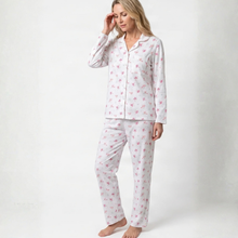 Load image into Gallery viewer, A woman modeling a two-piece pajama set with a white base and a pink floral pattern, standing against a plain white studio background.
