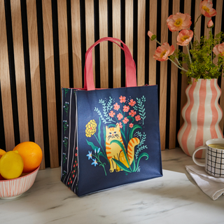 Navy tote bag with a cat and floral design on a wooden surface with a striped wall background.