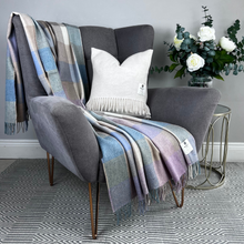Load image into Gallery viewer, Gray armchair with plaid blanket and decorative pillow, next to a small table with flowers.
