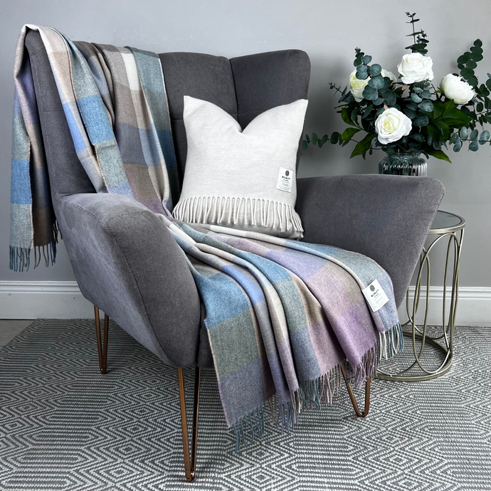 Gray armchair with plaid blanket and decorative pillow, next to a small table with flowers.