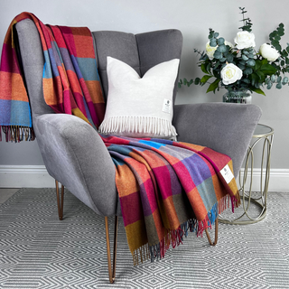 Gray armchair with a colorful plaid blanket and white pillow, next to a small table with flowers.
