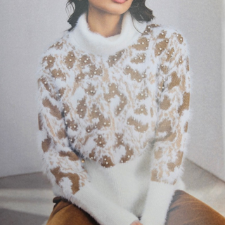 A woman wearing a fuzzy white mock-neck sweater with a brown leopard print pattern and small pearl embellishments, paired with brown leather pants.