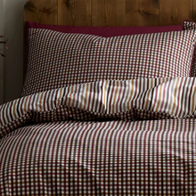 Load image into Gallery viewer, Checkered bedspread with striped pillow on a wooden headboard
