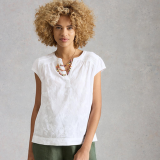Woman wearing a white sleeveless top with a textured pattern against a plain background