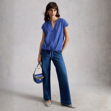 Load image into Gallery viewer, Full view of Model posing along with wearing the White Stuff Nicole Linen Blend Top in Bright Blue, with a grey background.
