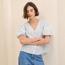 Load image into Gallery viewer, Woman wearing a light blue checkered blouse and blue jeans against a beige background
