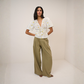Woman wearing a floral blouse and wide-leg pants against a plain background
