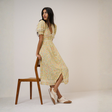 Load image into Gallery viewer, Woman in a floral dress sitting on a wooden chair against a plain background
