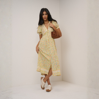 Woman wearing a floral dress holding a brown handbag against a white background