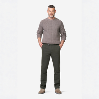 A man modeling a ribbed knit crewneck sweater in taupe and dark olive green trousers, standing against a plain white studio background.