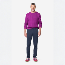 Load image into Gallery viewer, A man modeling a vibrant purple cable-knit crewneck sweater, paired with navy blue trousers and pink sneakers, standing against a plain white studio background.
