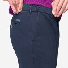 Load image into Gallery viewer, Close-up of a person wearing dark navy trousers, showing the back pocket, belt loop, and waistband, with hands adjusting the waist and a purple sweater visible at the top.
