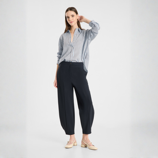A woman modeling a blue and white vertically striped button-down shirt paired with black wide-leg cropped pants and beige flat shoes, set against a plain light gray studio background.