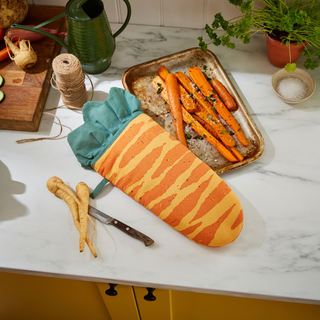 Carrot-shaped oven mitt on a kitchen counter with carrots and a knife.