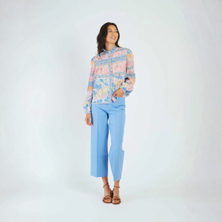 Woman wearing a colorful floral blouse and light blue pants on a white background