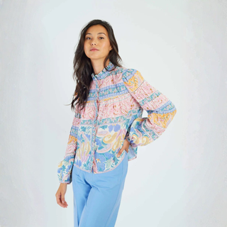Woman wearing a colorful patterned blouse with long sleeves on a white background