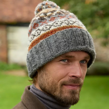 Load image into Gallery viewer, A man wearing a knit beanie hat with a gray ribbed brim and a multicolor patterned top section, photographed outdoors with a blurred green lawn and building in the background.
