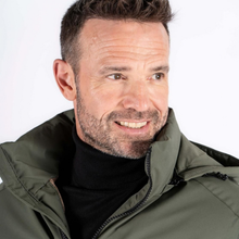 Load image into Gallery viewer, A close-up portrait of a smiling man wearing an olive green hooded jacket over a black turtleneck, set against a plain white background.
