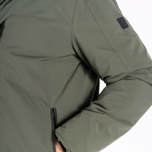 Load image into Gallery viewer, Close-up of an olive green technical jacket sleeve with a black zipper pocket and a small black brand patch on the upper arm, set against a plain white background.
