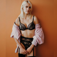 Load image into Gallery viewer, Fashion shot of a women wearing the Passionata Olivia Push Up Bra. Featuring the matching briefs and wearing a light pink jacket shrugged off the shoulder. 
