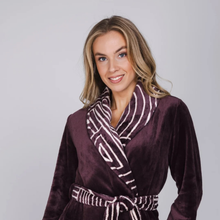 Load image into Gallery viewer, A woman wearing a plush bathrobe in deep plum purple with a contrasting white and purple striped patterned collar and tie belt, photographed against a solid light gray background.
