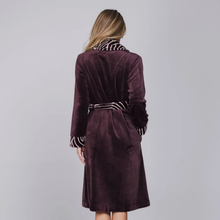Load image into Gallery viewer, A woman viewed from the back wearing a plush velvet robe in deep plum purple with contrasting black and white striped trim on the collar, cuffs, and belt.
