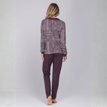 Load image into Gallery viewer, A woman viewed from behind wearing a matching two-piece loungewear set. The set features a long-sleeve top with a white and dark purple abstract wavy line pattern and solid dark purple cuffs, paired with solid dark purple pants.
