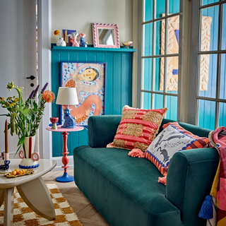 Colorful living room with teal sofa, colorful pillows, and a blue wall.
