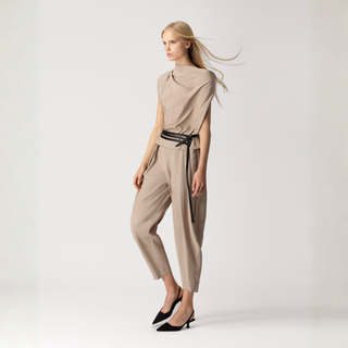 Woman wearing a beige jumpsuit with a black belt on a white background