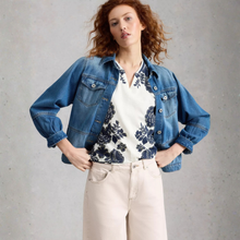 Load image into Gallery viewer, Woman wearing a denim jacket over a floral blouse with beige pants on a gray background
