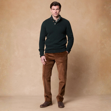 Load image into Gallery viewer, A man modeling a dark green knit polo sweater with a high collar, paired with brown corduroy trousers and brown leather boots, standing against a textured beige studio backdrop.
