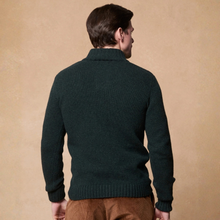 Load image into Gallery viewer, A man viewed from the back wearing a dark forest green ribbed knit sweater and brown trousers, standing against a textured beige background.
