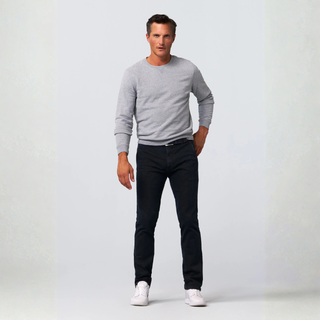 A man modeling a light gray long-sleeve crewneck sweater, dark slim-fit jeans, and white sneakers against a light gray studio background.