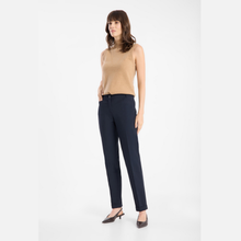 Load image into Gallery viewer, A woman modeling a sleeveless beige knit top and dark navy blue trousers, paired with dark brown slingback heels, against a plain light gray studio background.
