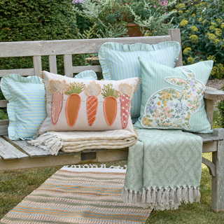 Decorative pillows with bunny and carrot designs on a wooden bench outdoors.