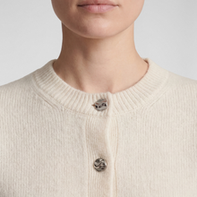 Load image into Gallery viewer, Close-up of a person wearing a cream-colored ribbed knit cardigan sweater with three decorative metallic buttons.
