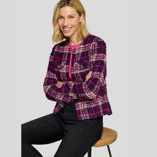 Woman wearing a patterned jacket sitting on a stool against a plain background