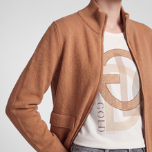 Load image into Gallery viewer, A close-up of a person wearing a ribbed knit zip-front cardigan in a warm camel brown over a white graphic T-shirt with a large beige and gold monogram design.
