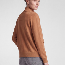 Load image into Gallery viewer, A woman wearing a camel brown knit mock neck cardigan, shown from a side-back angle against a light gray studio background.
