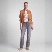 Load image into Gallery viewer, A model stands against a light gray studio background wearing a tan cropped jacket over a cream graphic T-shirt, gray jeans, and beige sneakers.
