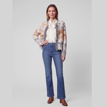 Load image into Gallery viewer, A woman stands against a light gray studio background wearing a cream blouse with a bow tie, a patterned cropped jacket in beige, orange, and gray tones, blue jeans, and brown ankle boots.
