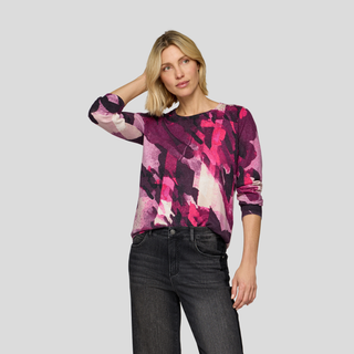 Woman wearing a colorful patterned top and black jeans on a light gray background